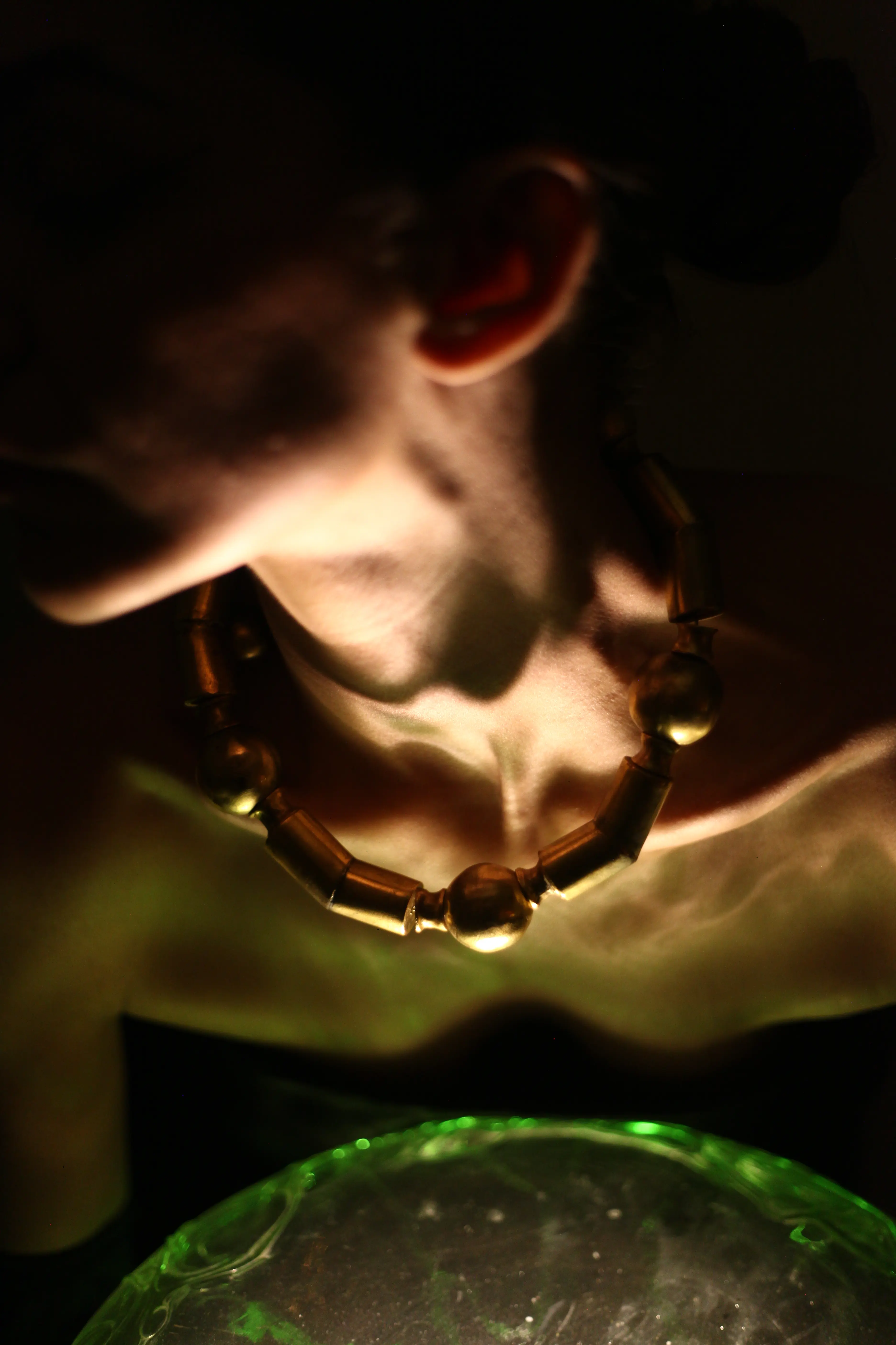 A brass necklace on the body, lit from below through glass